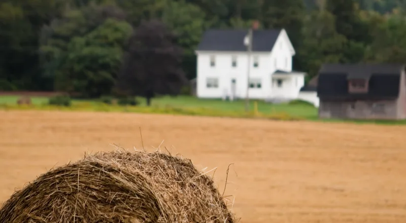 Hay bale in an open field with a white farmhouse in the background, Nasonworth, New Brunswick