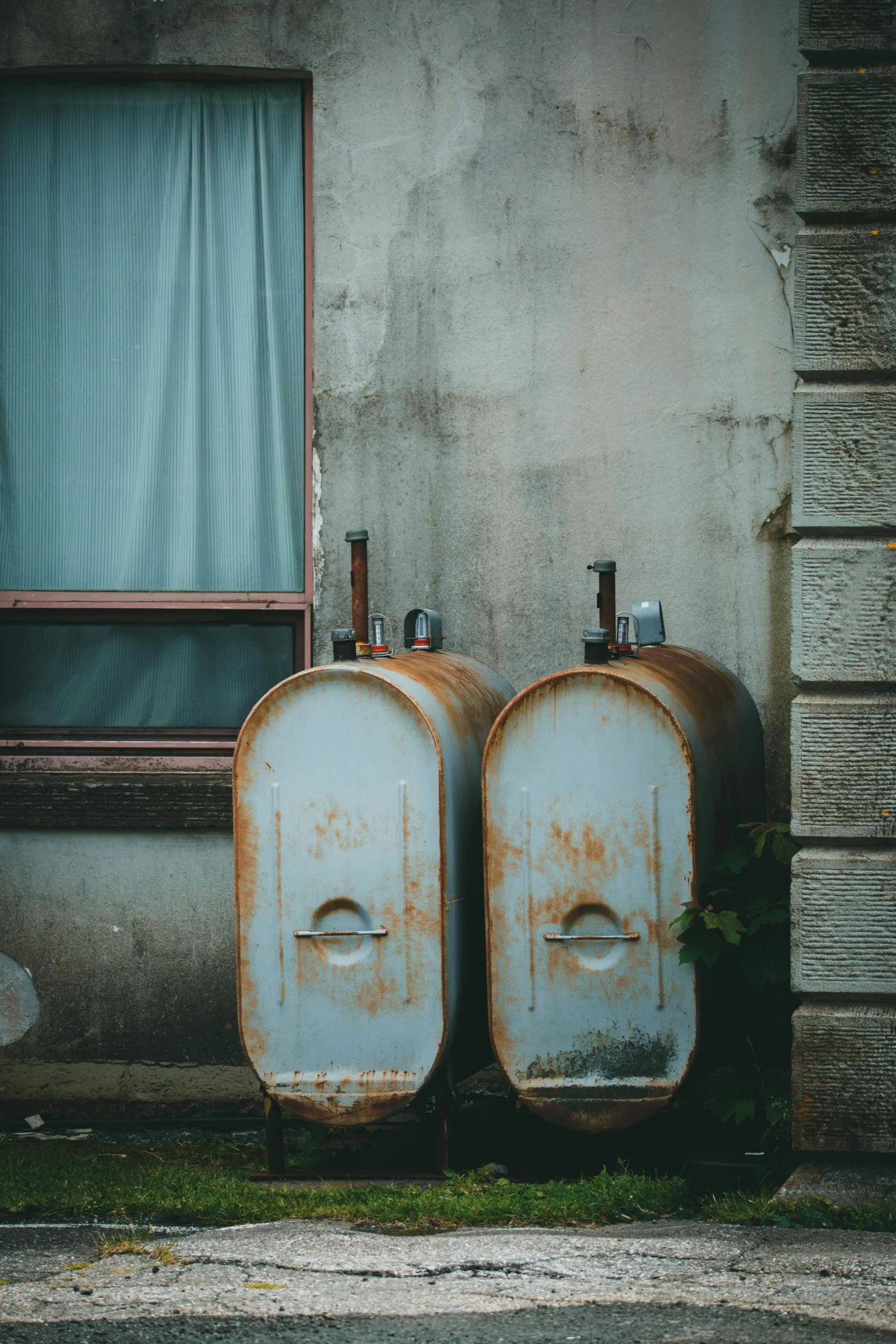 Two rusty outdoor oil tanks beside a home wall