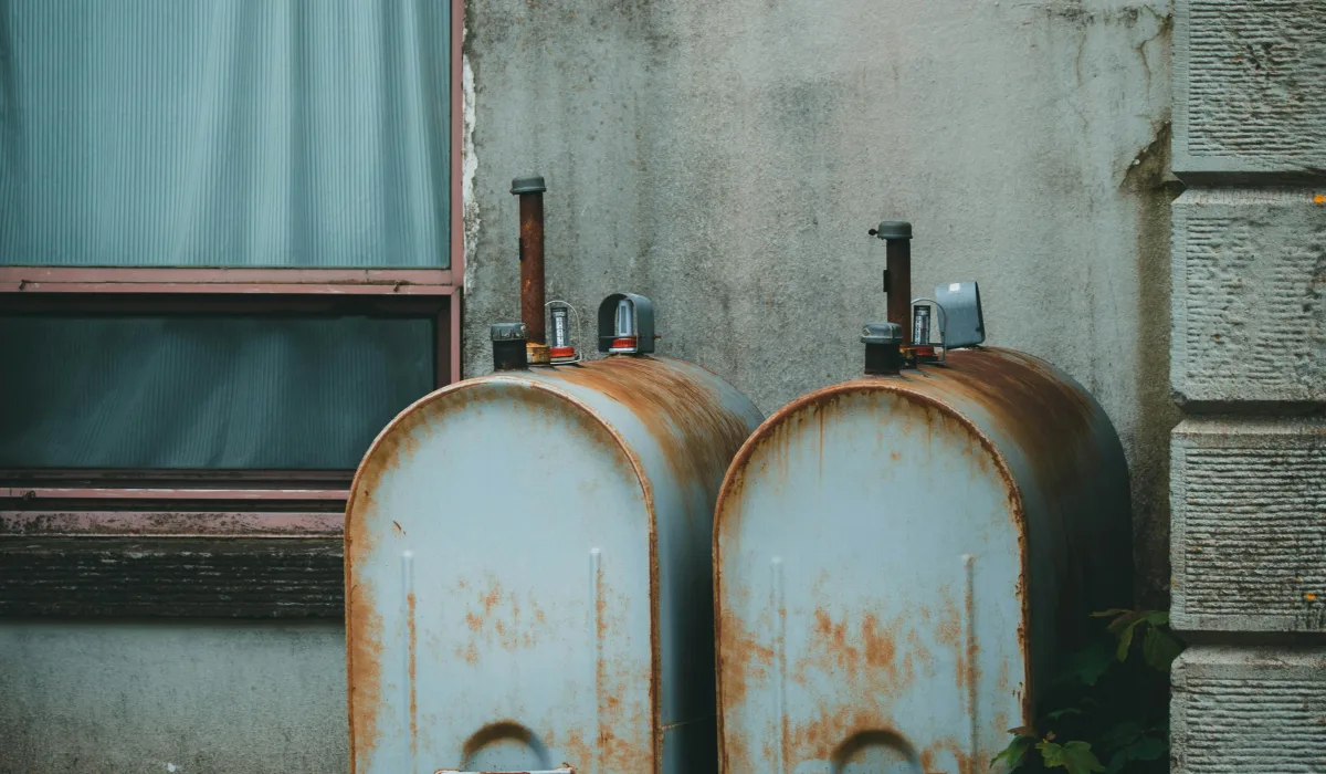 Two rusty outdoor oil tanks beside a home wall